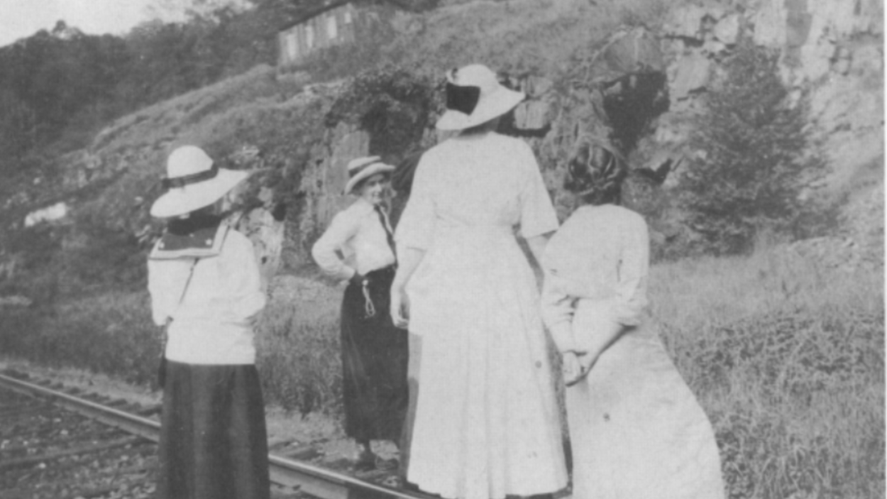 Four women standing on train tracks in front of a geologic otucrop.