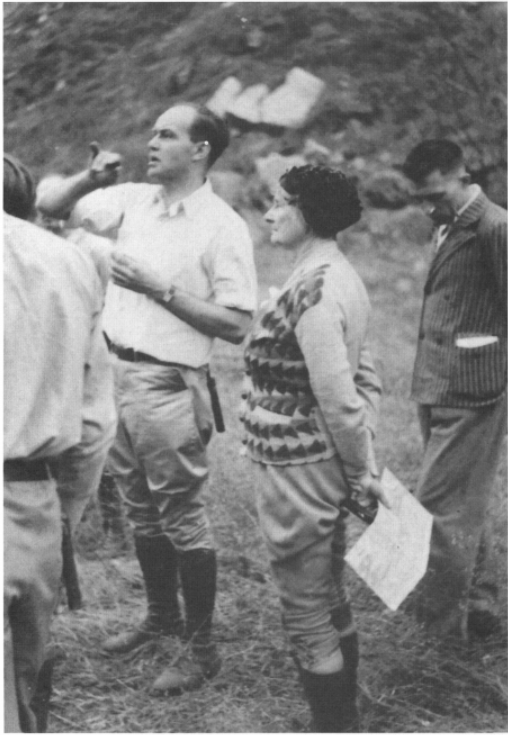 Florence Bascom with three other men in the field looking off to the distance. Bascom is holding a map and compass.