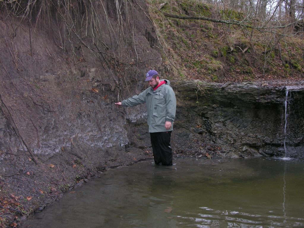 Image of me standing in cold water next to a rock outcrop illustrating fieldwork difficulties.