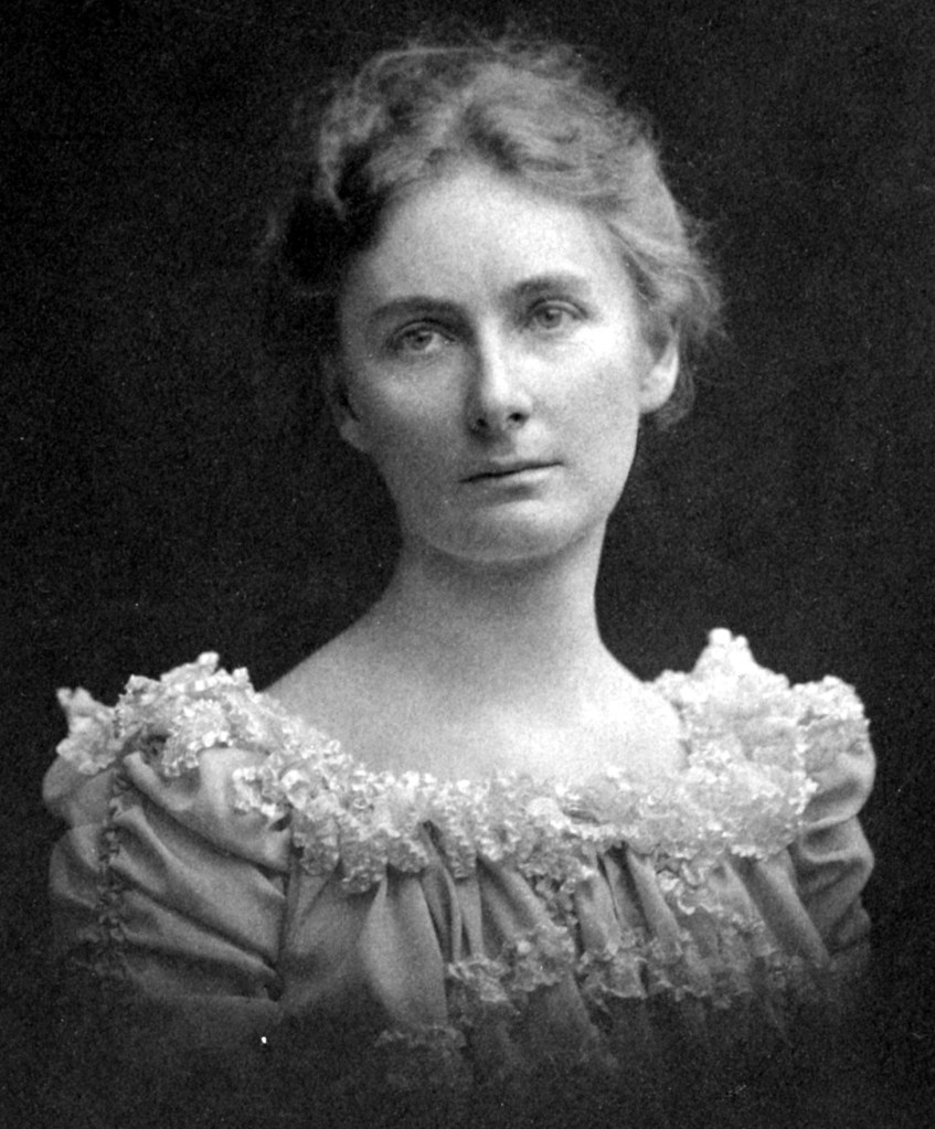 A portrait of a young woman with short wavy hair waring an older style, frilly dress